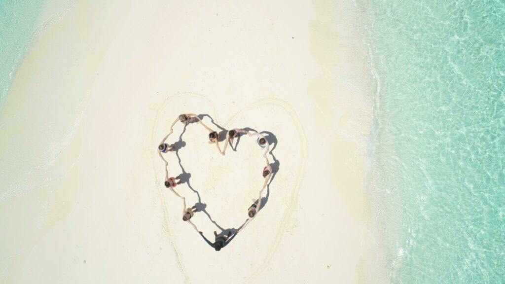 People form the shape of a heart on the beach.